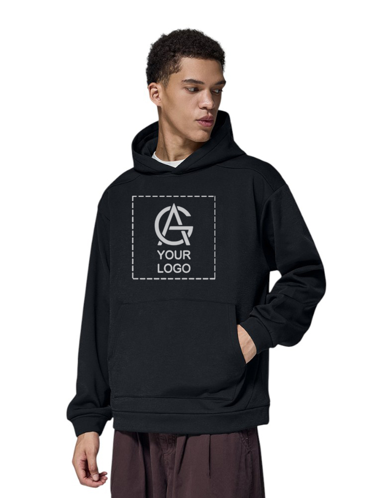 A person wearing a black hoodie with a customizable logo area on the front, featuring "YOUR LOGO" text inside a dashed square. The person has one hand in the hoodie pocket and is looking to the side.