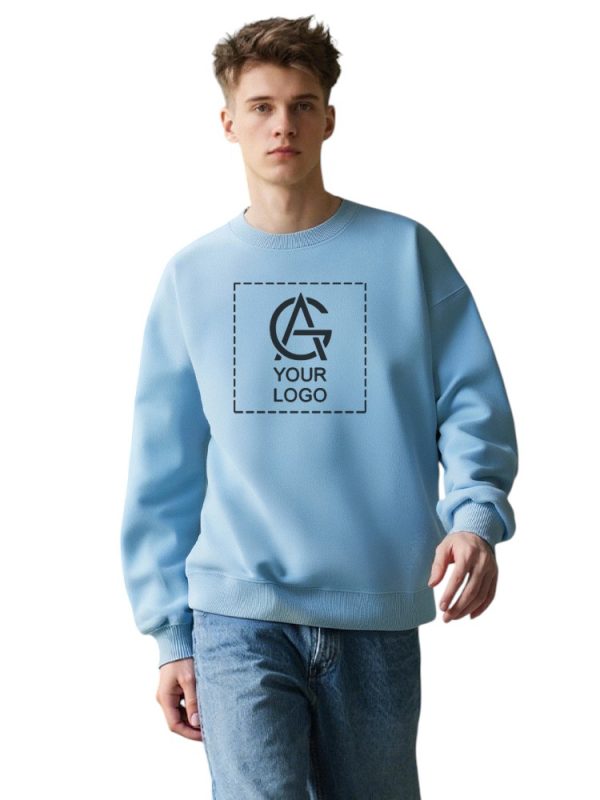 A young person wearing a light blue sweatshirt with a placeholder square and the text "YOUR LOGO" printed on the front, paired with blue jeans, standing against a plain white background.