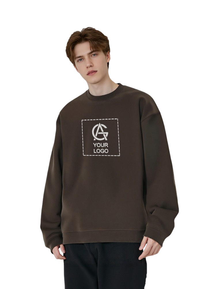 A young man with short brown hair wears a loose, dark brown sweatshirt displaying a placeholder logo and the words "YOUR LOGO" in a white, dashed box. He stands against a plain white background.