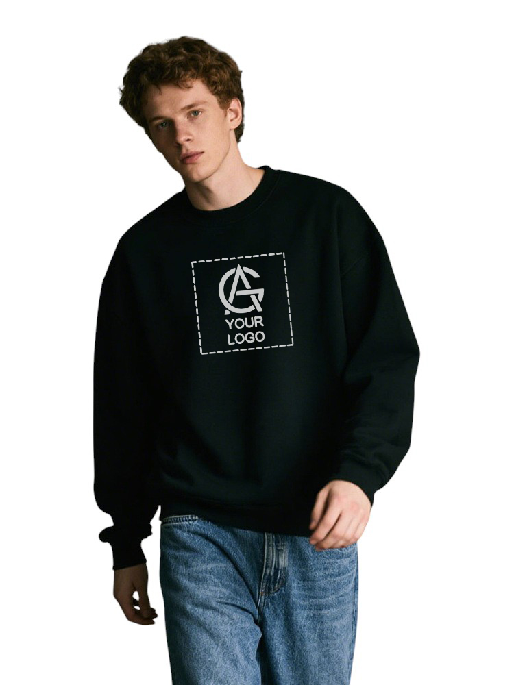 A young man with curly hair wears a black sweatshirt with a square logo area reading "YOUR LOGO" in white text, and blue jeans, standing against a plain white background.