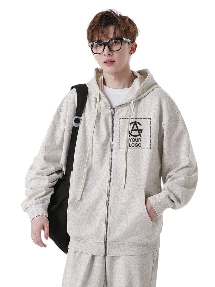 A young person with short brown hair and glasses wears a light gray zip-up hoodie with a "YOUR LOGO" design on the chest, matching pants, and a black shoulder bag, posing with one hand in their pocket.