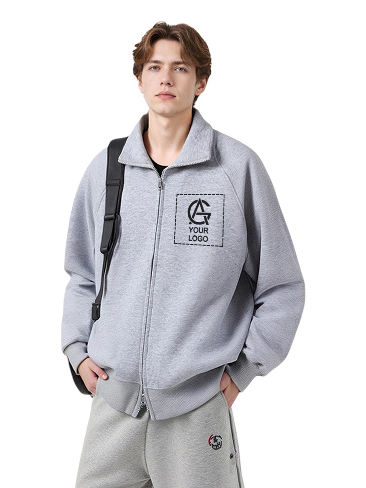 A young man wearing a light gray zip-up jacket with a black "Your Logo" design on the chest and matching gray sweatpants, standing with one hand in his pocket and a black shoulder bag.