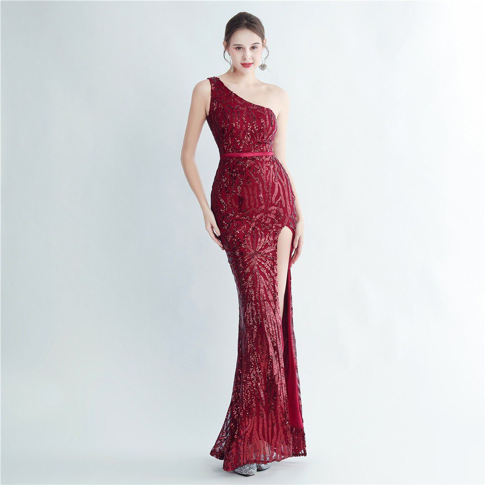 Model wearing a burgundy sequin one-shoulder gown with a thigh-high slit