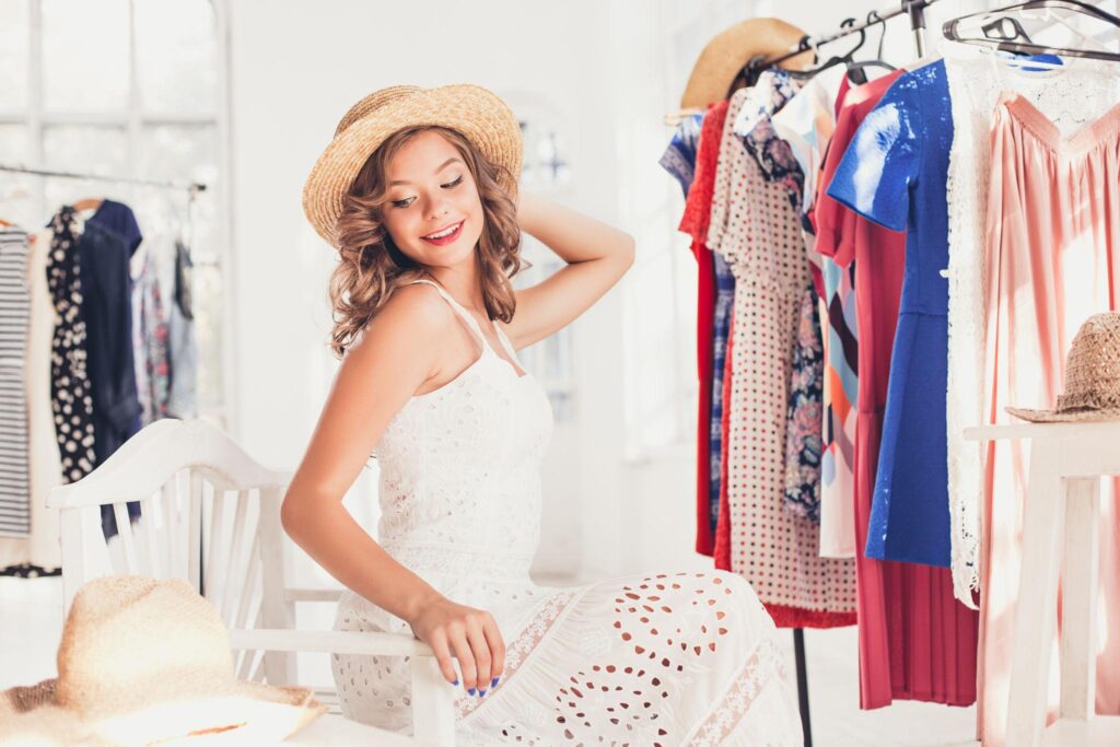 Young woman wearing a beige hat and standing behind a rack of colorful women's clothing